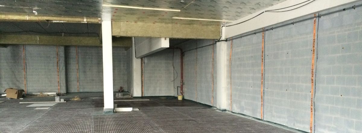 unfinished basement with concrete walls and floor. A structural column and exposed beams are visible, basement membrane installation