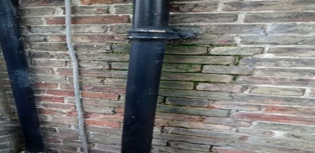 A leaking, blocked downpipe causing water ingress and damp patches on exterior brickwork
