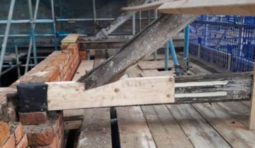 Exposed construction site with wooden beams and brickwork, where new epoxy resin timber support is attached to an old beam