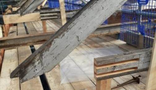 Close-up of wooden beams and planks, requiring timber resin repair, in a construction or renovation site, with scaffolding and blue safety rails visible in the background.