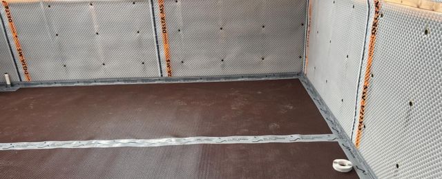 waterproofing membrane on the floor, white panels on walls, and wooden window frame