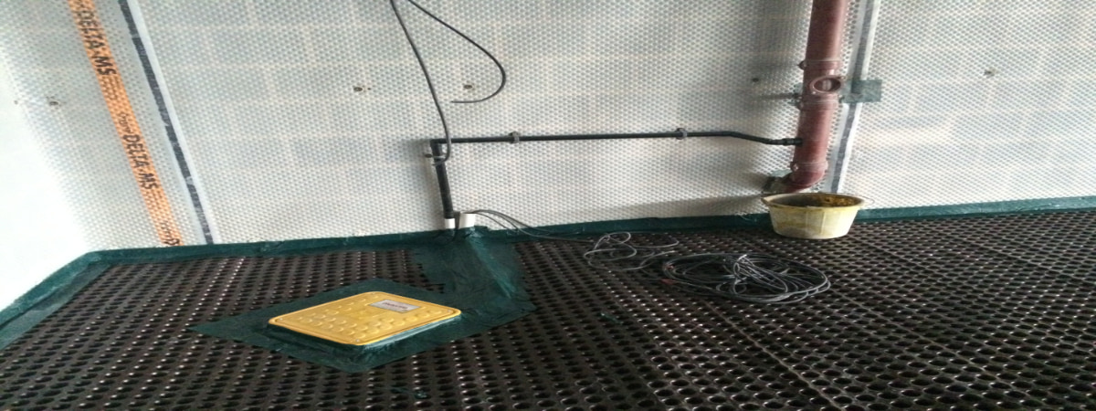 Installation of a basement waterproofing system featuring a black studded floor and wall membrane (DELTA-MS). The central focus is the yellow access cover for a buried sump pump basin, highlighting the crucial collection point for a primary or backup sump pump system.
