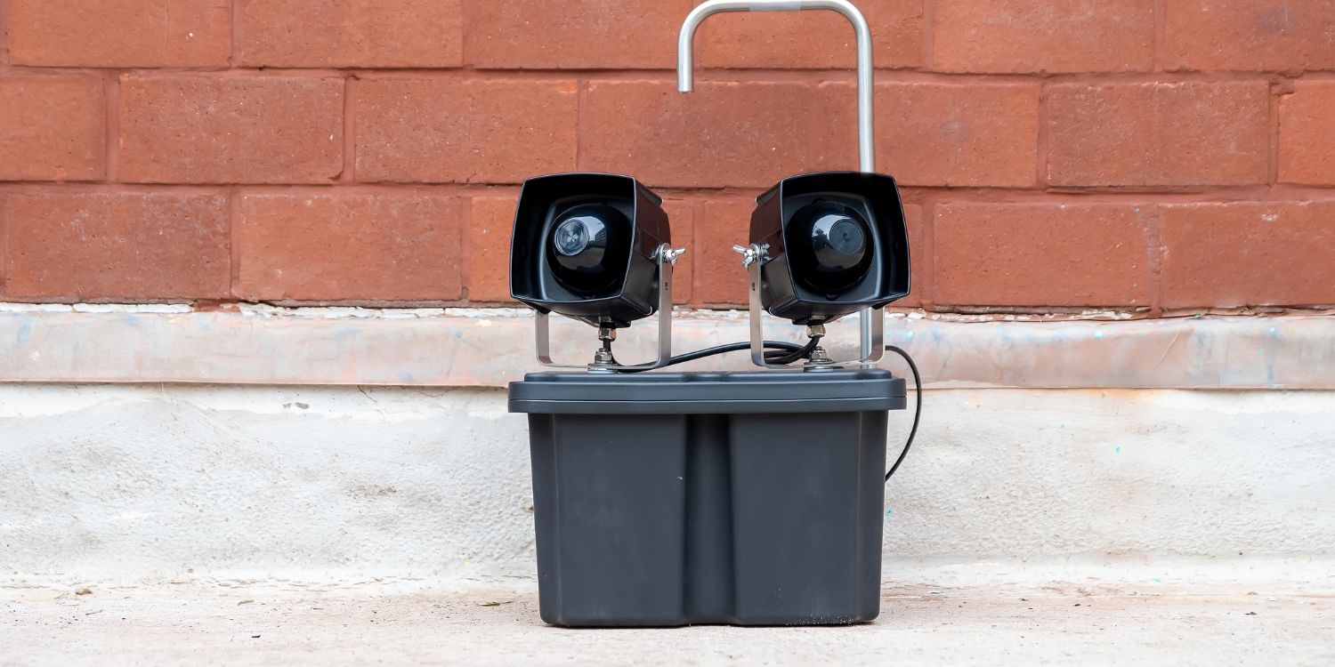 Dual-speaker sonic bird chaser device installed on a roof against a brick wall to deter birds using distress calls and predatory sounds.